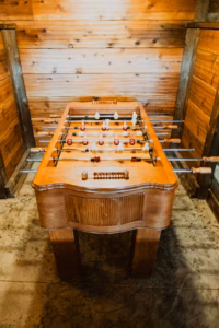 A wooden foosball table with player rods in a room with wooden walls and a stone floor.