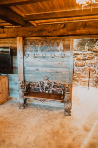 A rustic wooden bench with carved bear figures beneath a wall featuring horse cutouts and coat hooks in a cabin-style room with exposed wooden beams and stone walls.