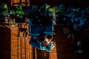 Overhead view of a couple embracing on a wooden floor next to a long, decorated table set with greenery and floral arrangements.