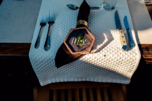 Place setting with a white textured placemat, cutlery, black napkin with gold ring, and a hexagonal name card reading "Marie Schultz.
