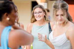A group of women stand together and talk at a Horstmann Homestead wedding, with one woman in glasses smiling at the camera while others are engaged in conversation.