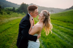 A bride and groom embrace and smile at each other in a grassy field with rolling hills in the background during their Horstmann Homestead wedding.