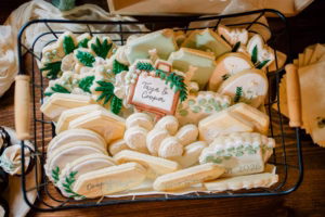 A basket filled with assorted decorated cookies, including plaques, leaves, and geometric shapes—some adorned with names, dates, and sweet nods to a Horstmann Homestead wedding celebrating love and tradition.